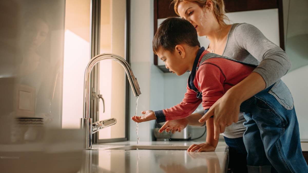 Mother helping child wash hands in kitchen sink